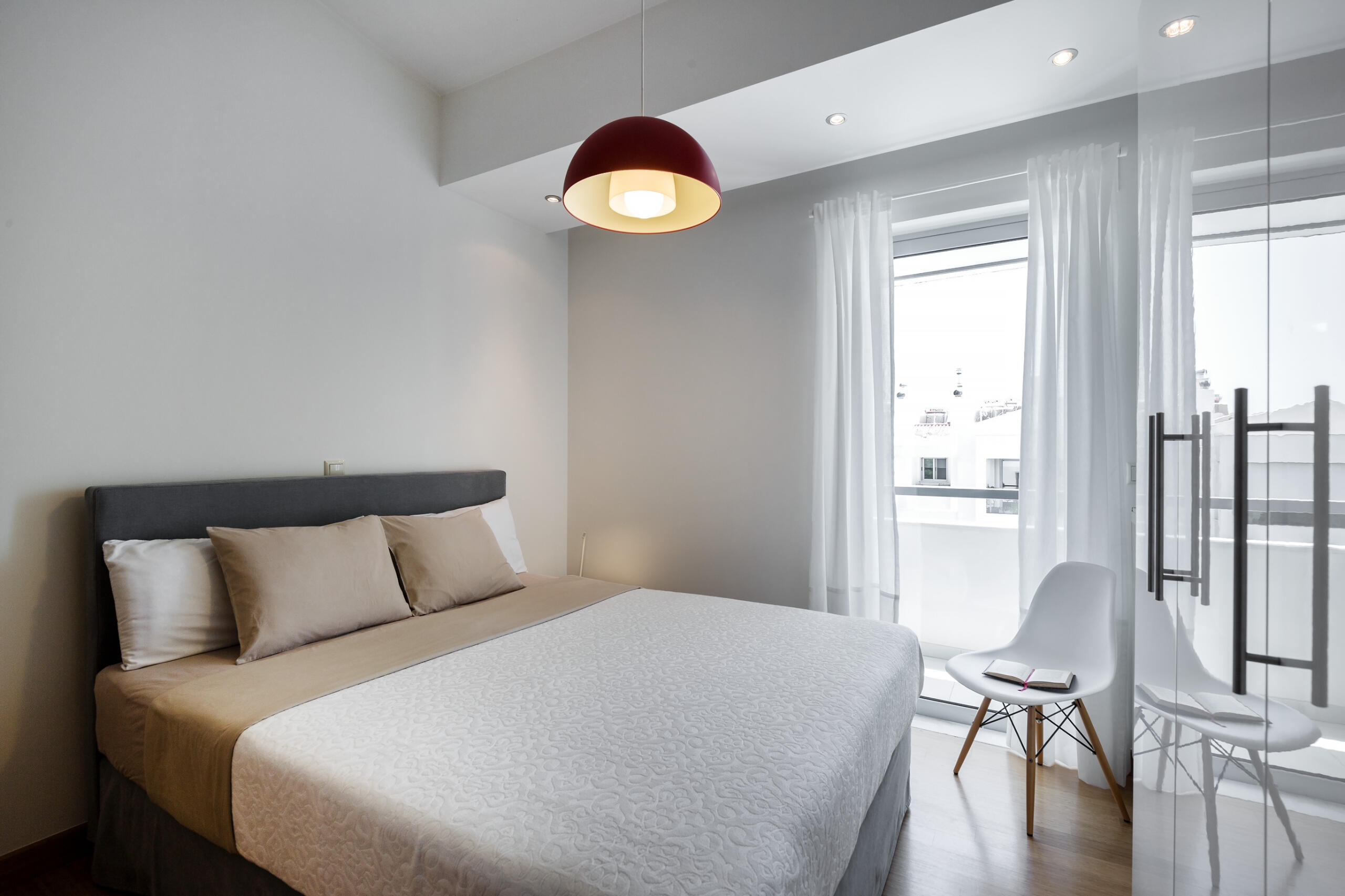 Μίνιμαλ υπνοδωμάτιο με γκρι υφασμάτινο κρεβάτι και λευκή ντουλάπα και καρέκλα σε καθαρές γραμμές. Minimal bedroom with a grey fabric bed and white wardrobe and chair in clean, simple lines.