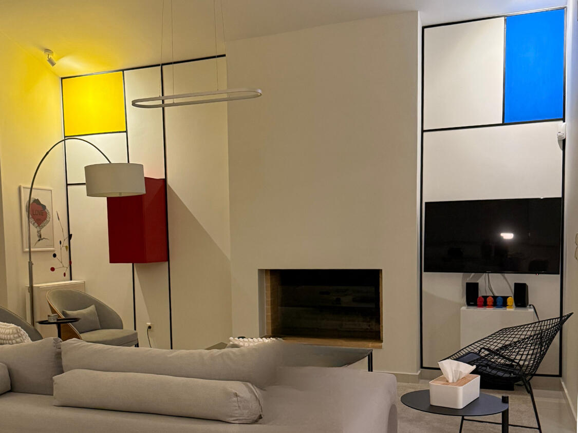 Εσωτερικό αθηναϊκού διαμερίσματος που συνδυάζει τη μοντέρνα αισθητική με τη ζεστασιά, διαθέτοντας τζάκι και τηλεόραση ενσωματωμένα σε τοίχο με στοιχεία Mondrian, αναδεικνύοντας τη γεωμετρική αρμονία του χώρου. Interior of an Athenian apartment blending mod
