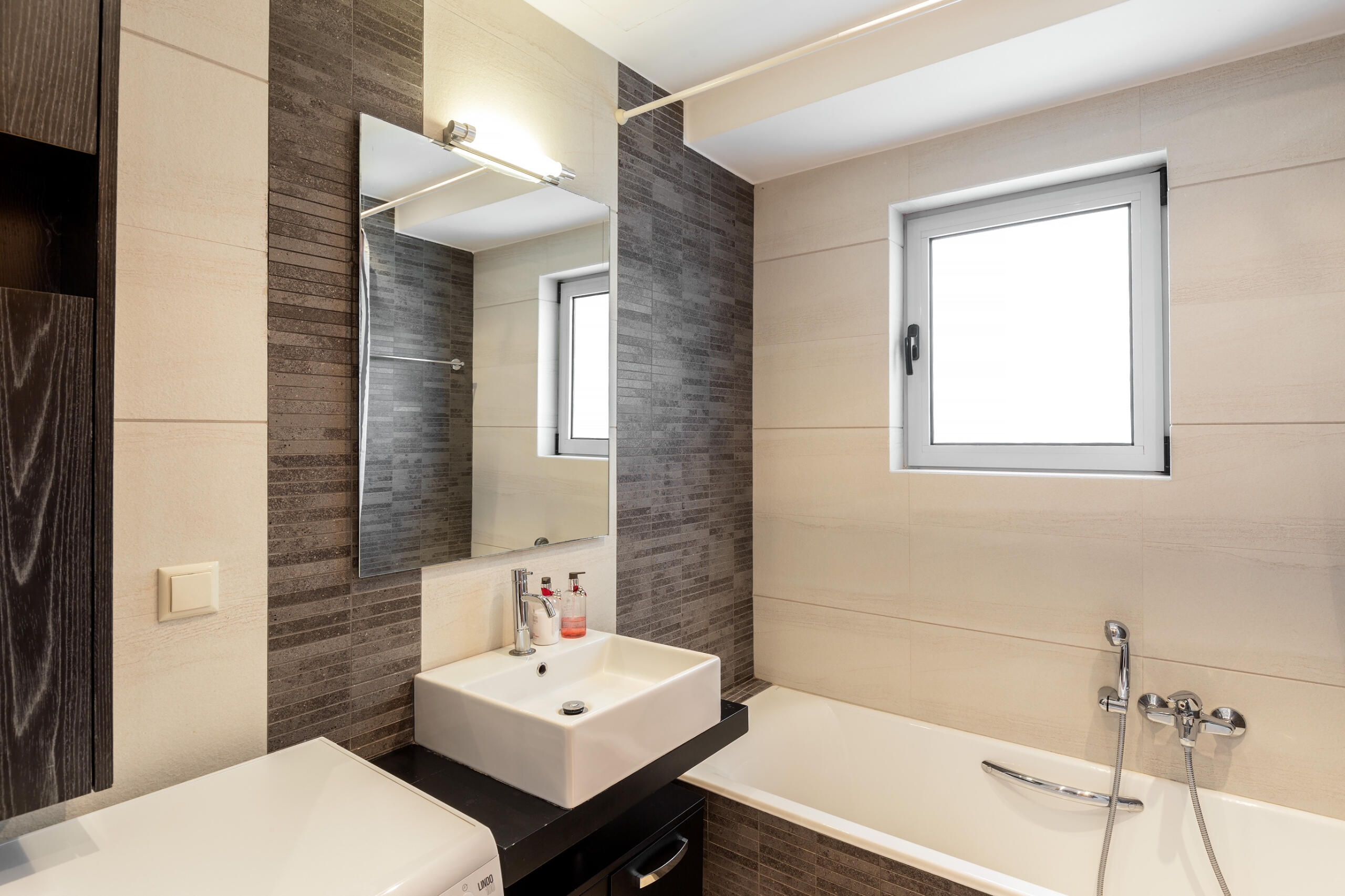 Μοντέρνο μπάνιο με γκρι πλακίδια, minimal σχεδιασμό και ουδέτερη χρωματική παλέτα. Modern bathroom with grey tiles, minimal design, and a neutral color palette.